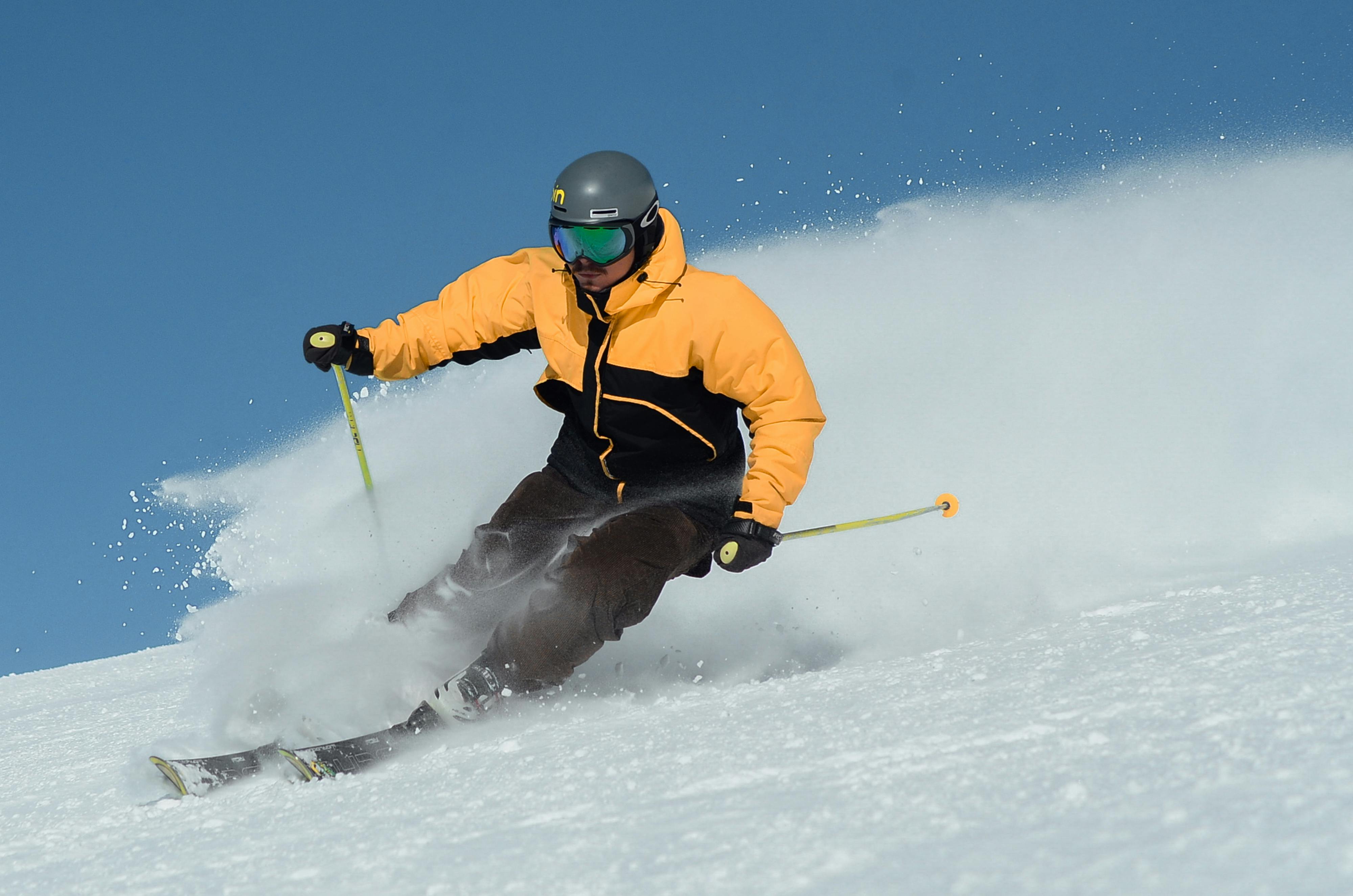 Image of a man skiing in an yellow and black jacket with black skiing pants